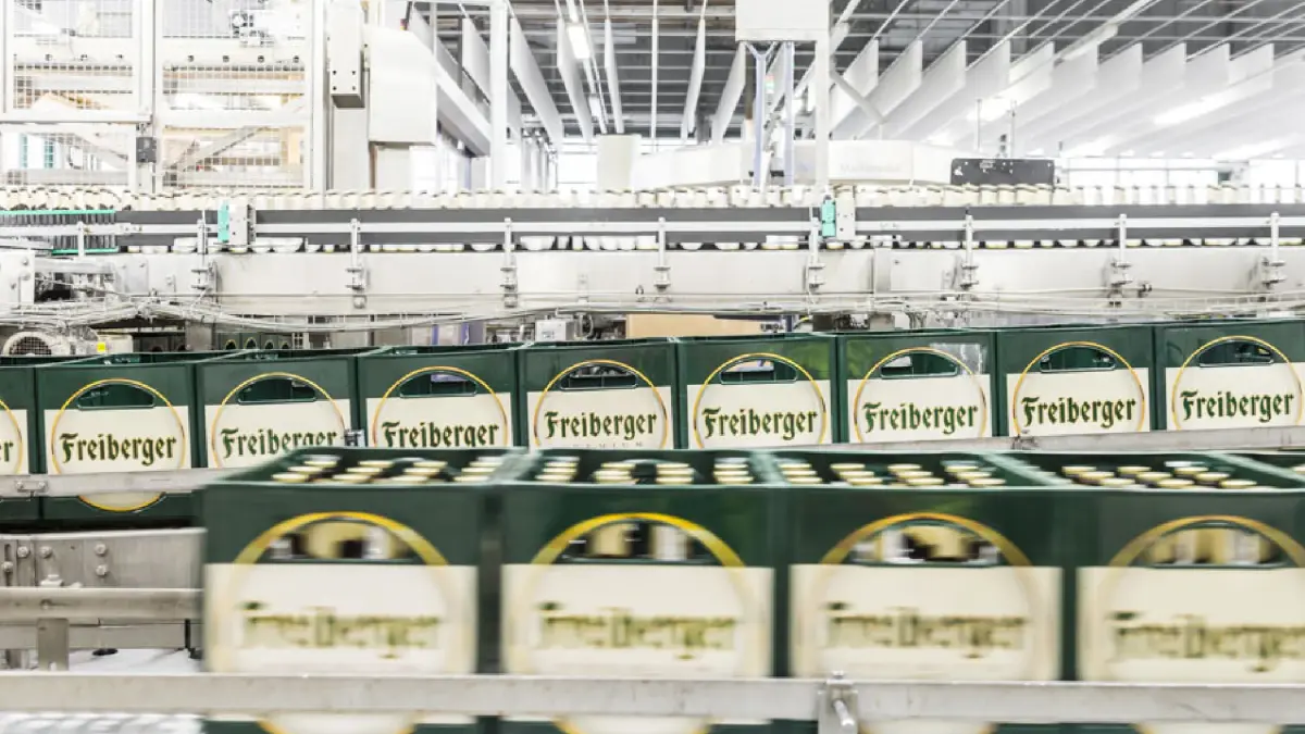 Grüne Kisten auf einem Förderband in einer Fabrikhalle sind gestapelt.