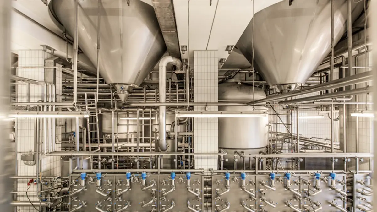 Große Edelstahltanks und ein Netzwerk aus Rohrleitungen dominieren eine moderne Industrieanlage.