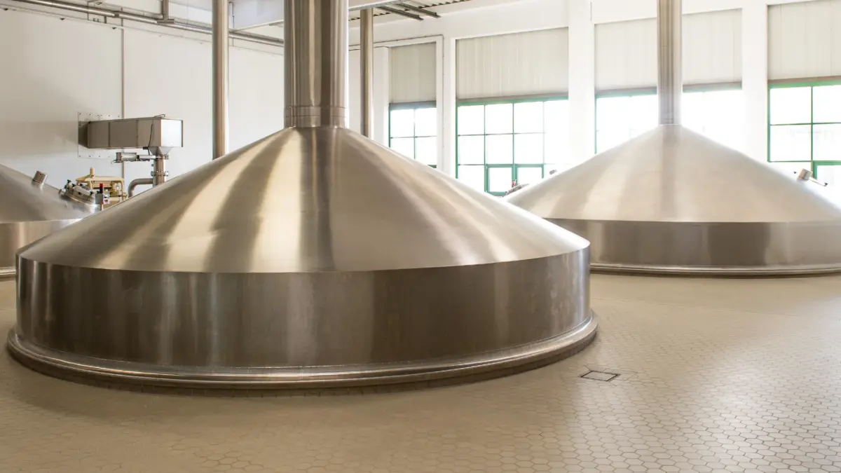 Zwei große, metallene Braukessel stehen in einer industriellen Brauereihalle.