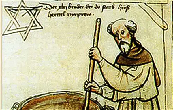 Älterer bärtiger Mann in Mönchskleidung steht neben einem runden Tisch mit einem Stern im Hintergrund.