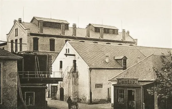 Historische Schwarz-Weiß-Aufnahme einer Gebäudeanlage mit gepflastertem Hof und Pferdewagen.