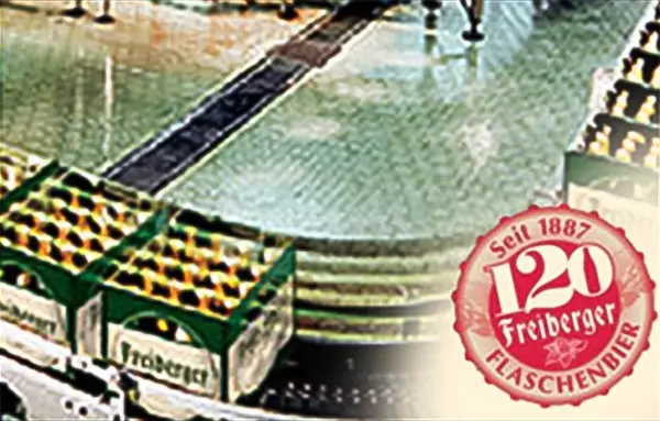 Bierflaschen bewegen sich auf einem Förderband in einer Fabrik. Ein rotes Siegel ist im Vordergrund zu sehen.