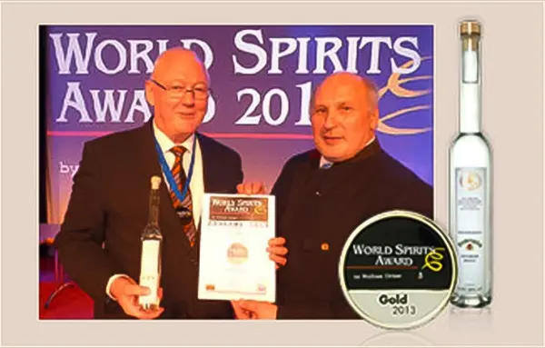 Zwei Herren stehen auf einer Bühne und halten eine Auszeichnung sowie eine Flasche.