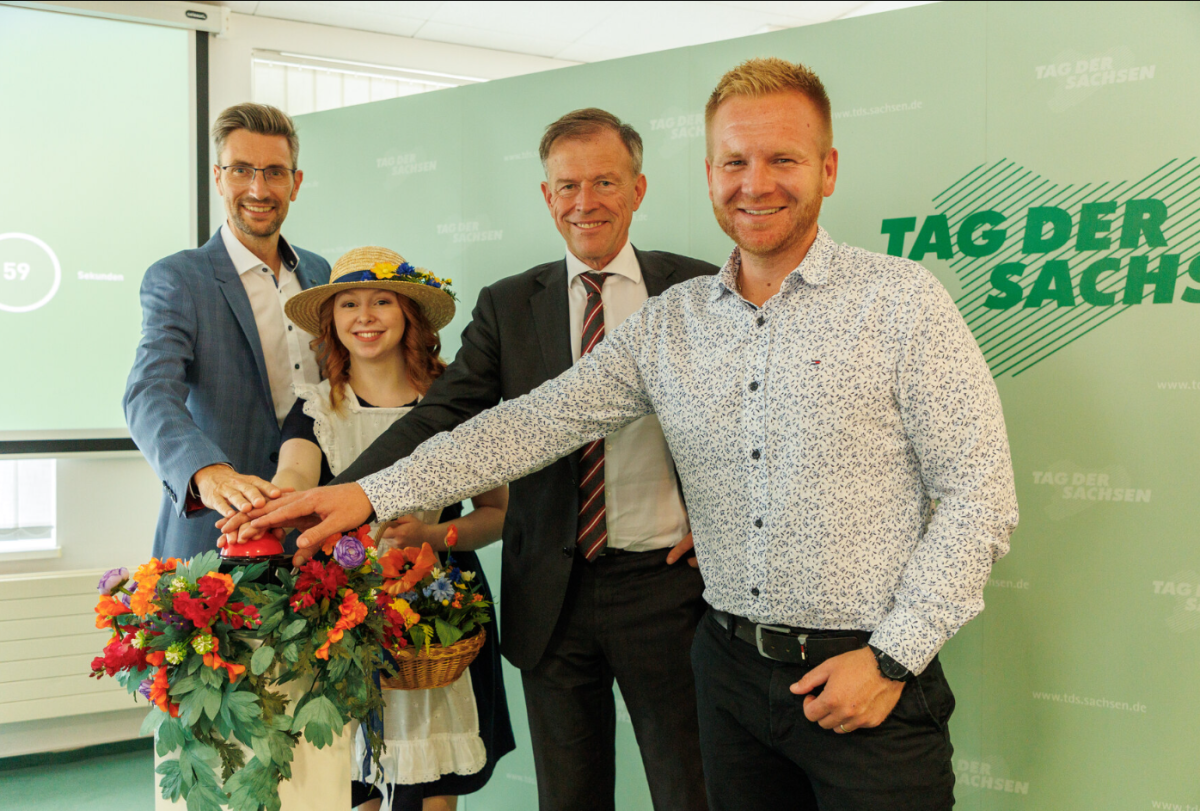 Eine Gruppe von 4 Menschen stehen vor einer Werbetafel und halten ihre Hände über ein Blumenbouqet