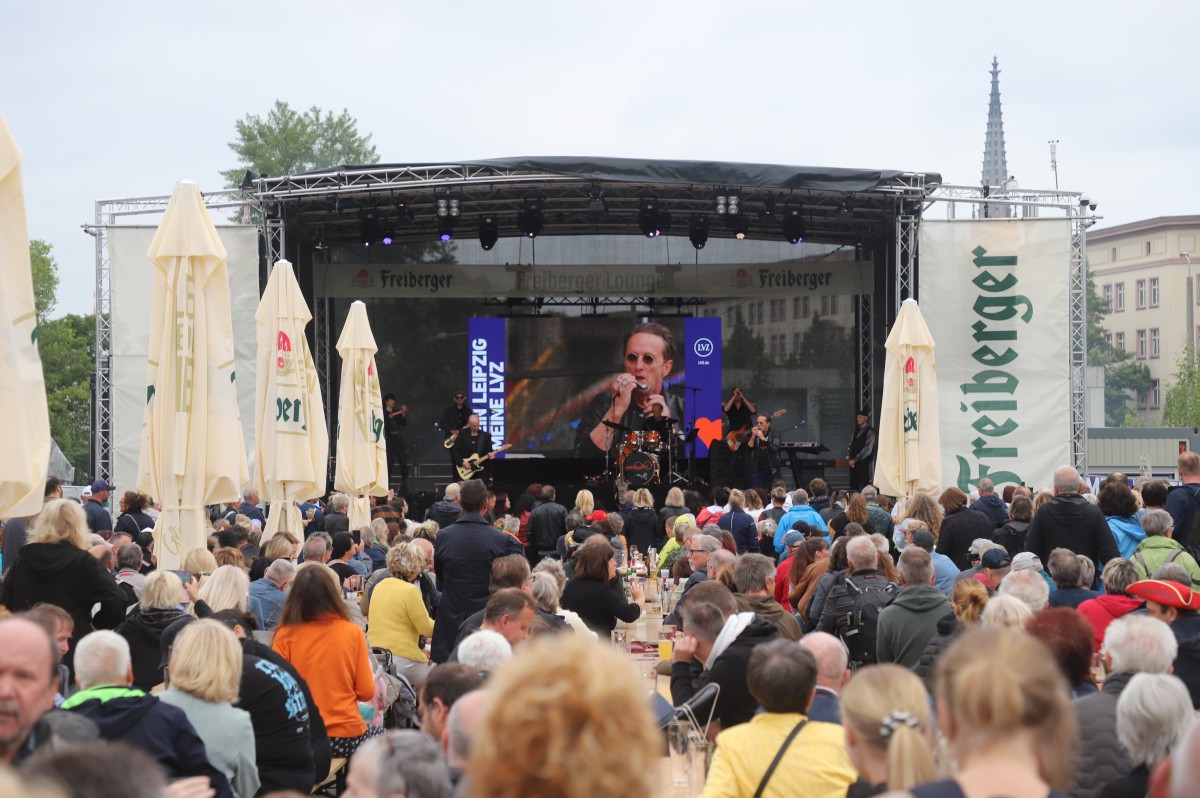 Viele Menschen sitzen vor einer Bühne an Tischen, auf der Bühne spielt eine Band.