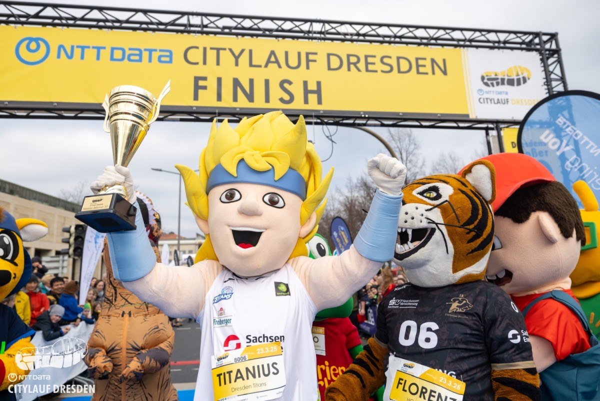 Verschiedene Maskottchen Figuren stehen unter dem Zieleinlauf des Citylauf Dresden.
