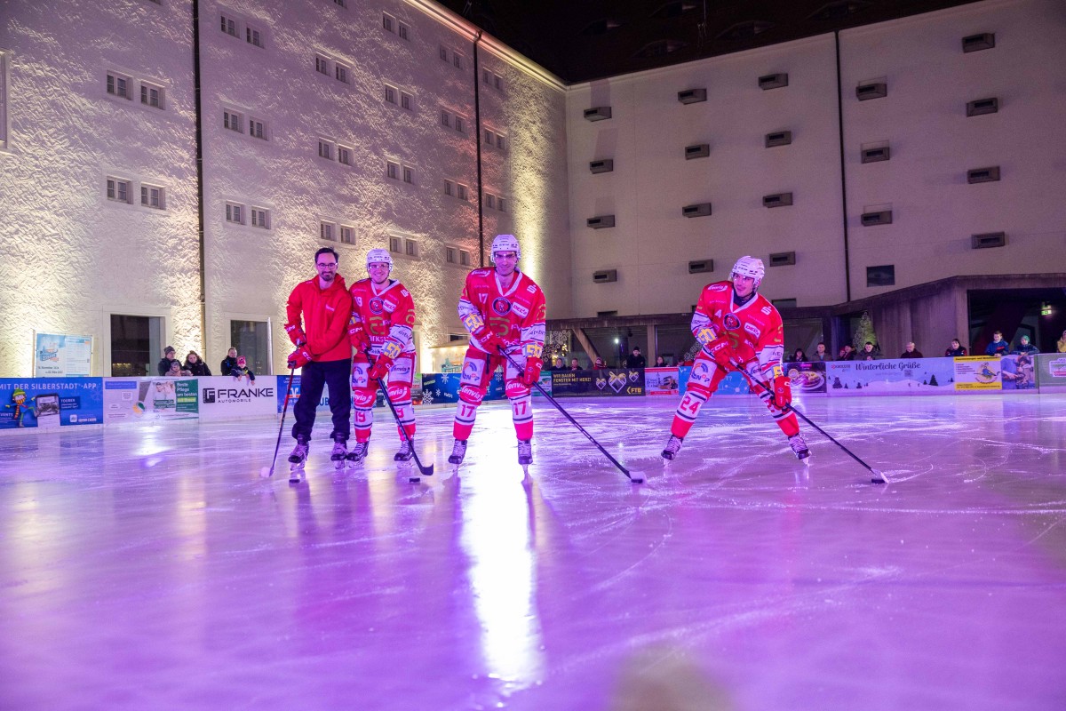 Vier Eishockey Spieler mit Eishockeyschlägern stehen auf dem Eis, dahinter Zuschauer an der Bande.