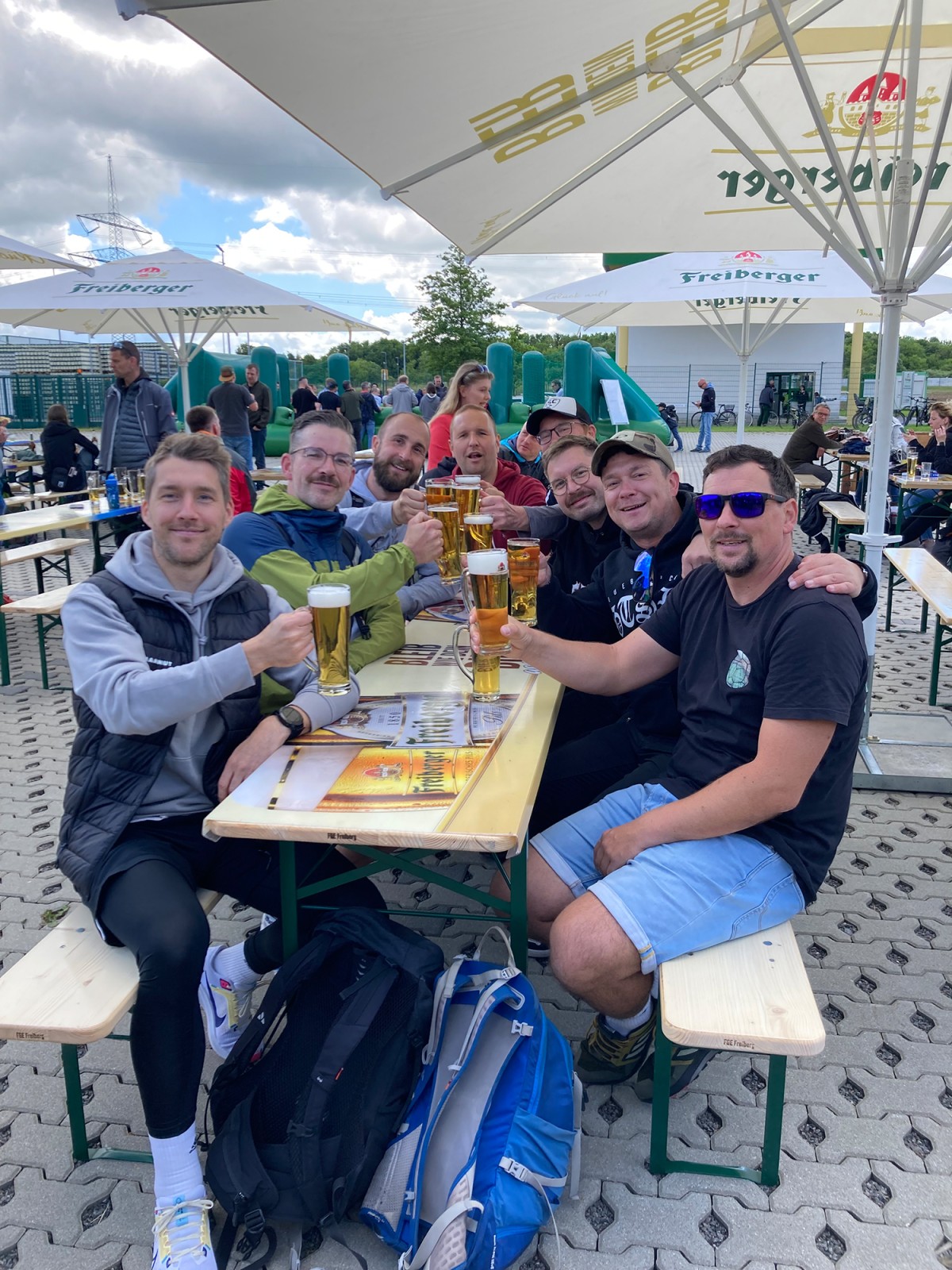 Eine Gruppe Menschen sitzt unter einem Schirm und stößt mit gefüllten Freiberger Biergläsern an.