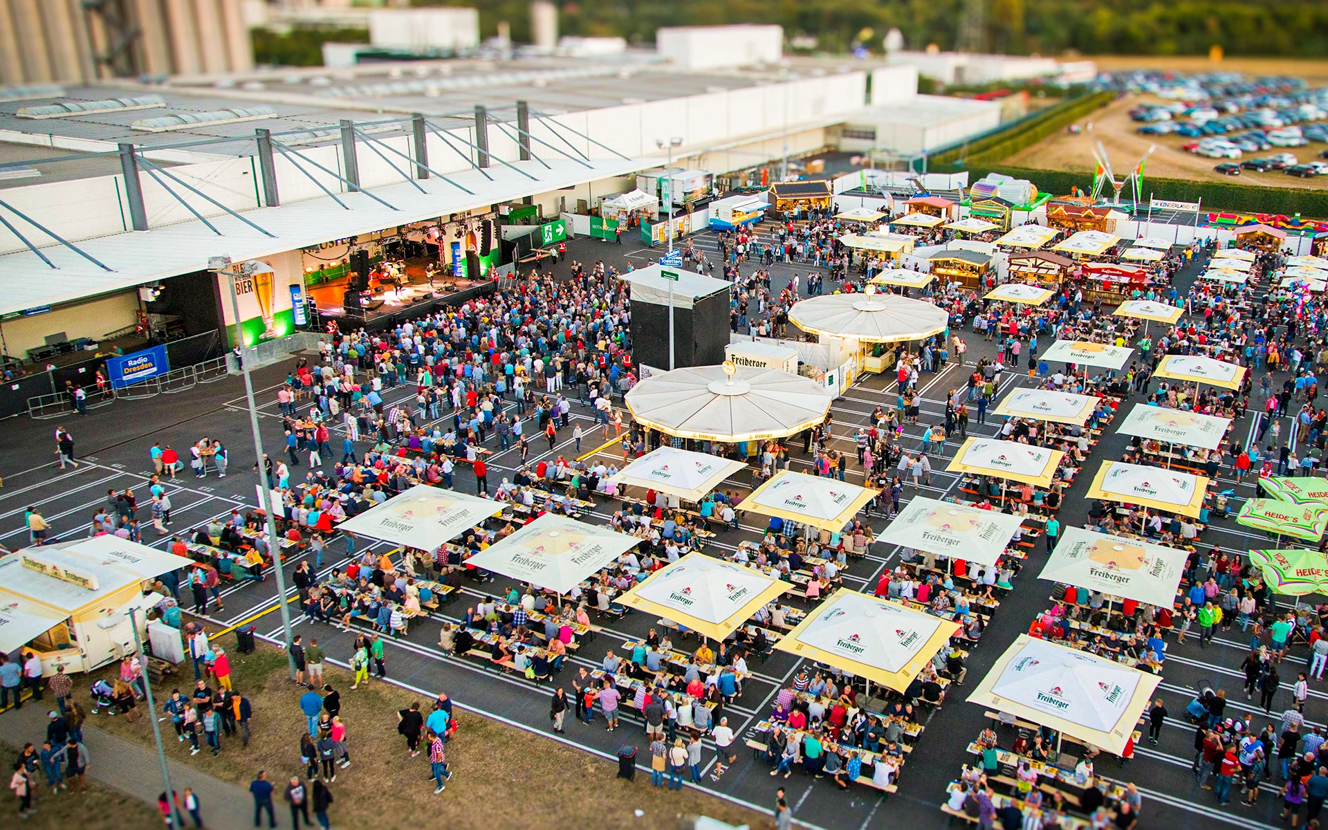 Großes Freiluftfest mit Bühnenbereich und vielen Tischen unter Freiberger-Sonnenschirmen. Im Hintergrund Industriehallen und Parkplätze.