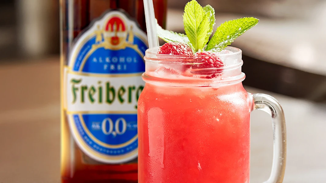 Ein rotes Getränk in einem Glas mit Henkel ist garniert mit Pfefferminzblättern und Himbeeren.