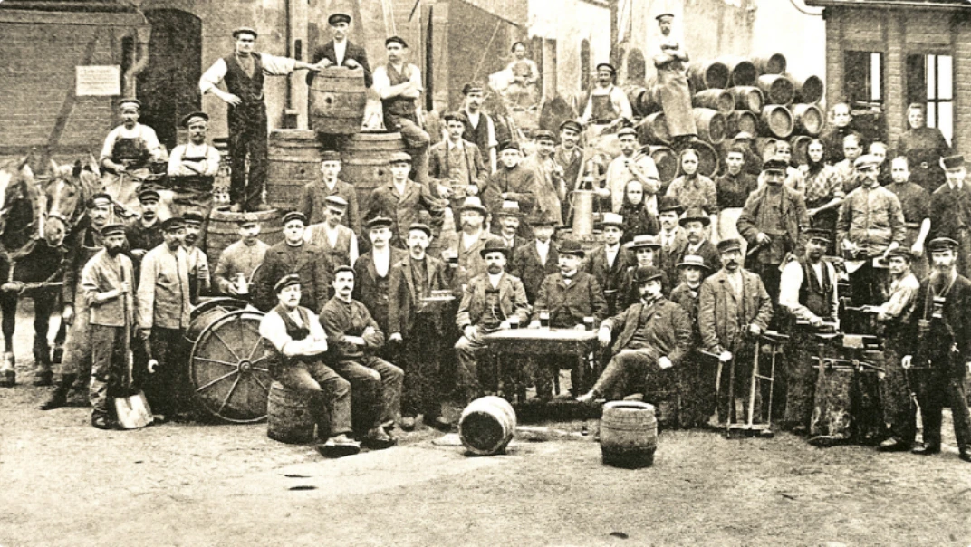Historisches Foto zeigt eine Gruppe von Arbeitern mit Fässern und Ausrüstung vor einem Lagerhaus.