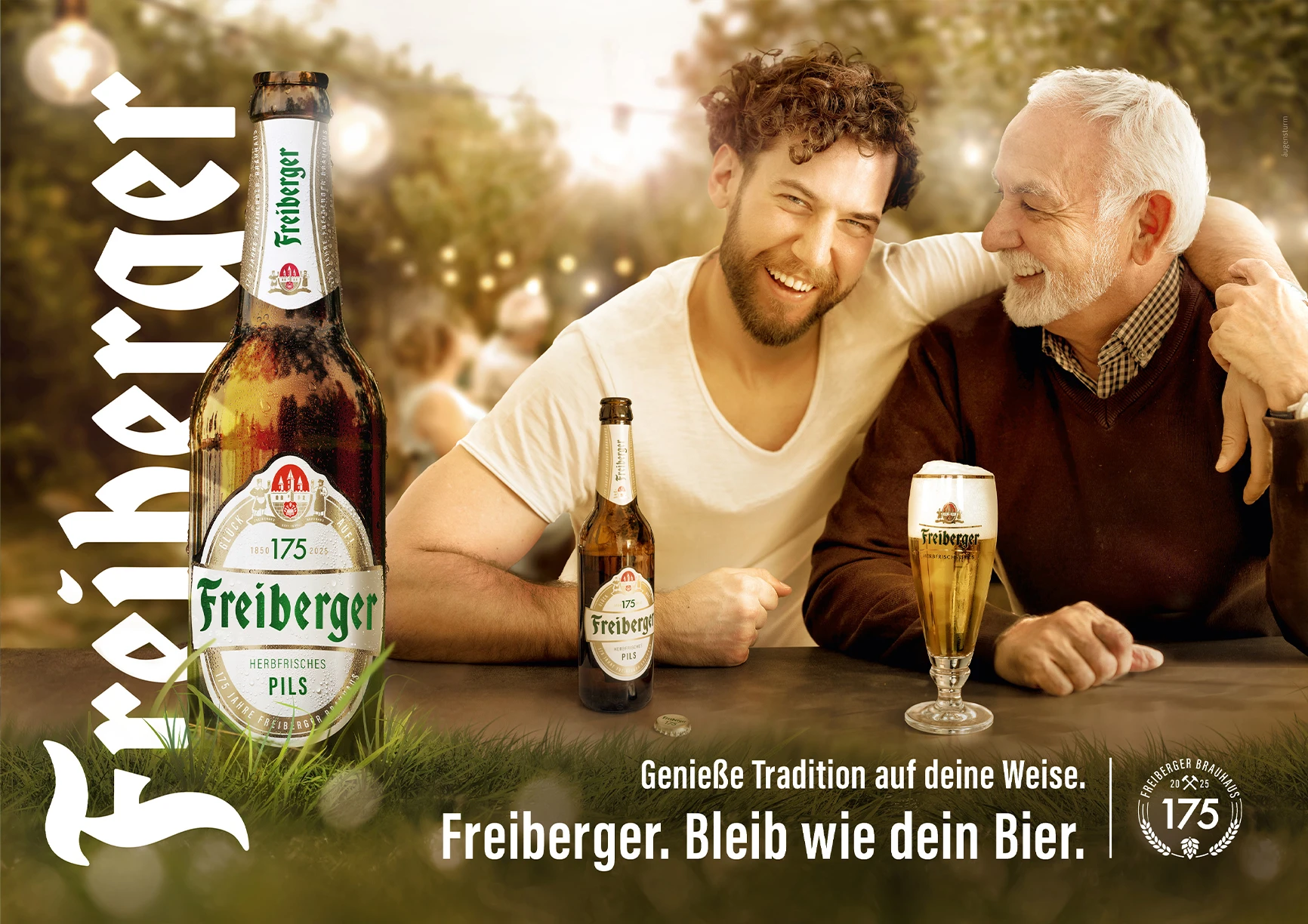 Ein älterer und ein jüngerer Mann lächeln, sitzen zusammen an einem Tisch mit Bieren.