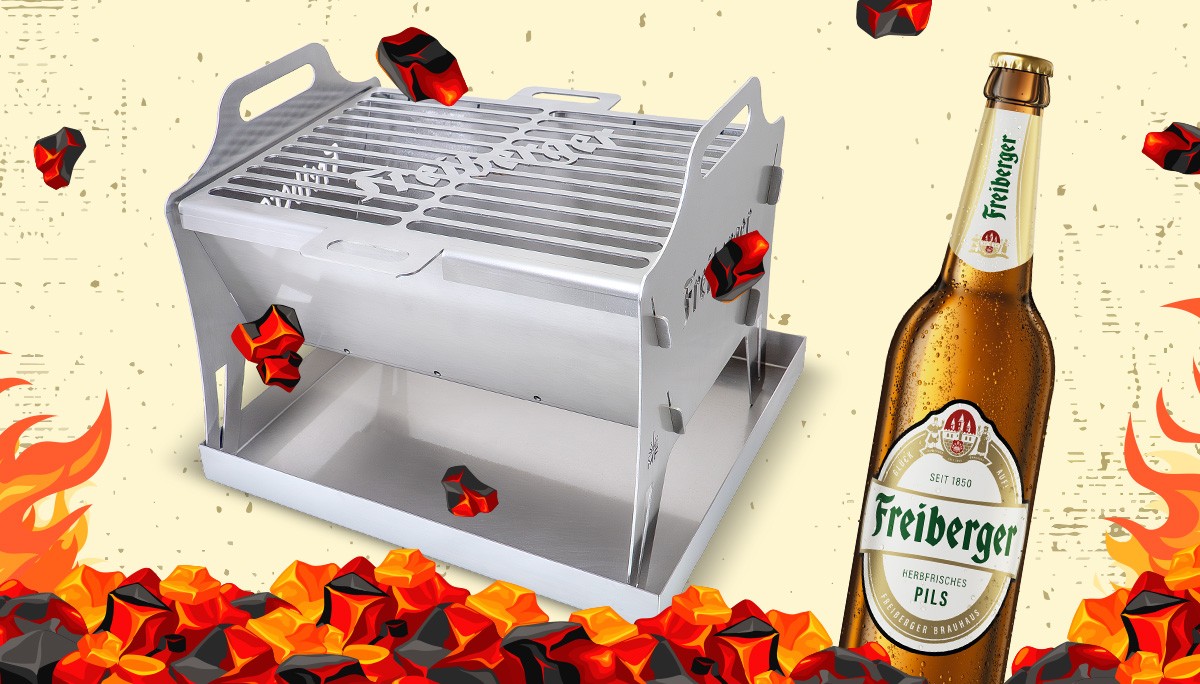 Ein modularer Grill steht auf gelben Untergrund neben einer Freiberger Flasche, darumter Grillkohle.